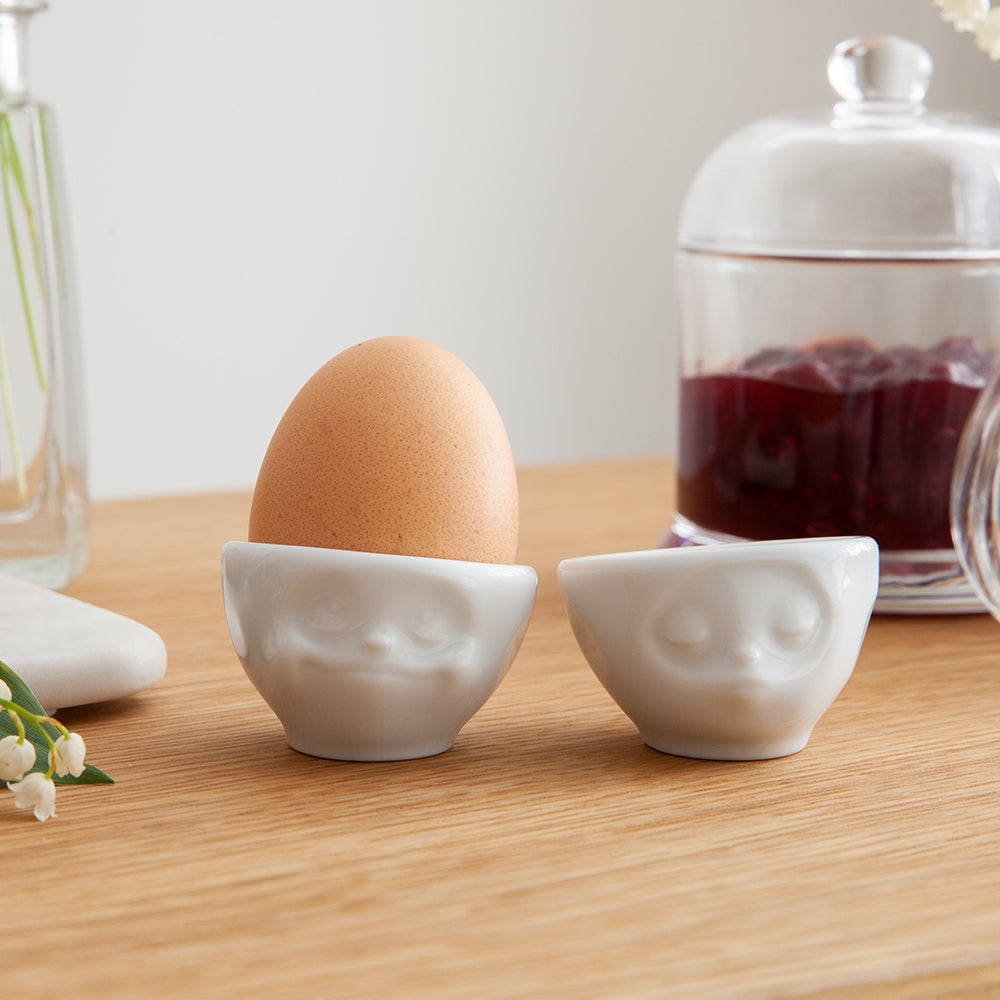Set of two egg cups in white from the porcelain product family of fun dishware by FIFTYEIGHT Products. Set features two egg cups in white, featuring 'kissing' and 'dreamy' facial expressions. Dishwasher and microwave safe bowls. Shipped in exclusively designed gift box.