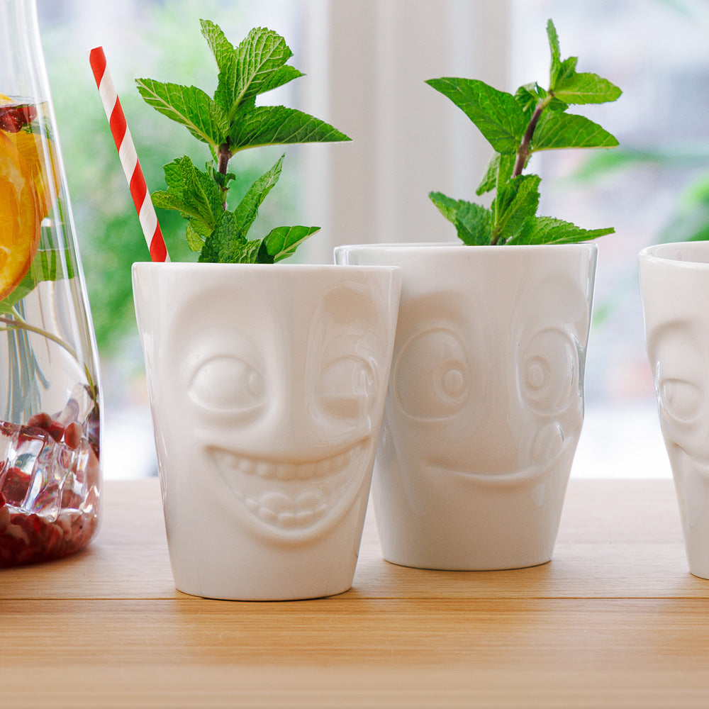 Set of two coffee mugs without handles in white from the porcelain product family of fun dishware by FIFTYEIGHT Products. Each offering 11 oz capacity. Dishwasher and microwave safe coffee cups with a 'joking' and one with a 'tasty' facial expression. Shipped in exclusively designed gift box.