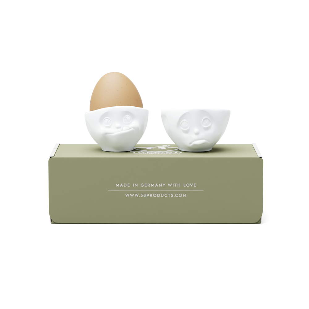 Set of two egg cups in white from the porcelain product family of fun dishware by FIFTYEIGHT Products. Set features two egg cups in white, featuring 'Oh please' and 'tasty' facial expressions. Dishwasher and microwave safe bowls. Shipped in exclusively designed gift box.