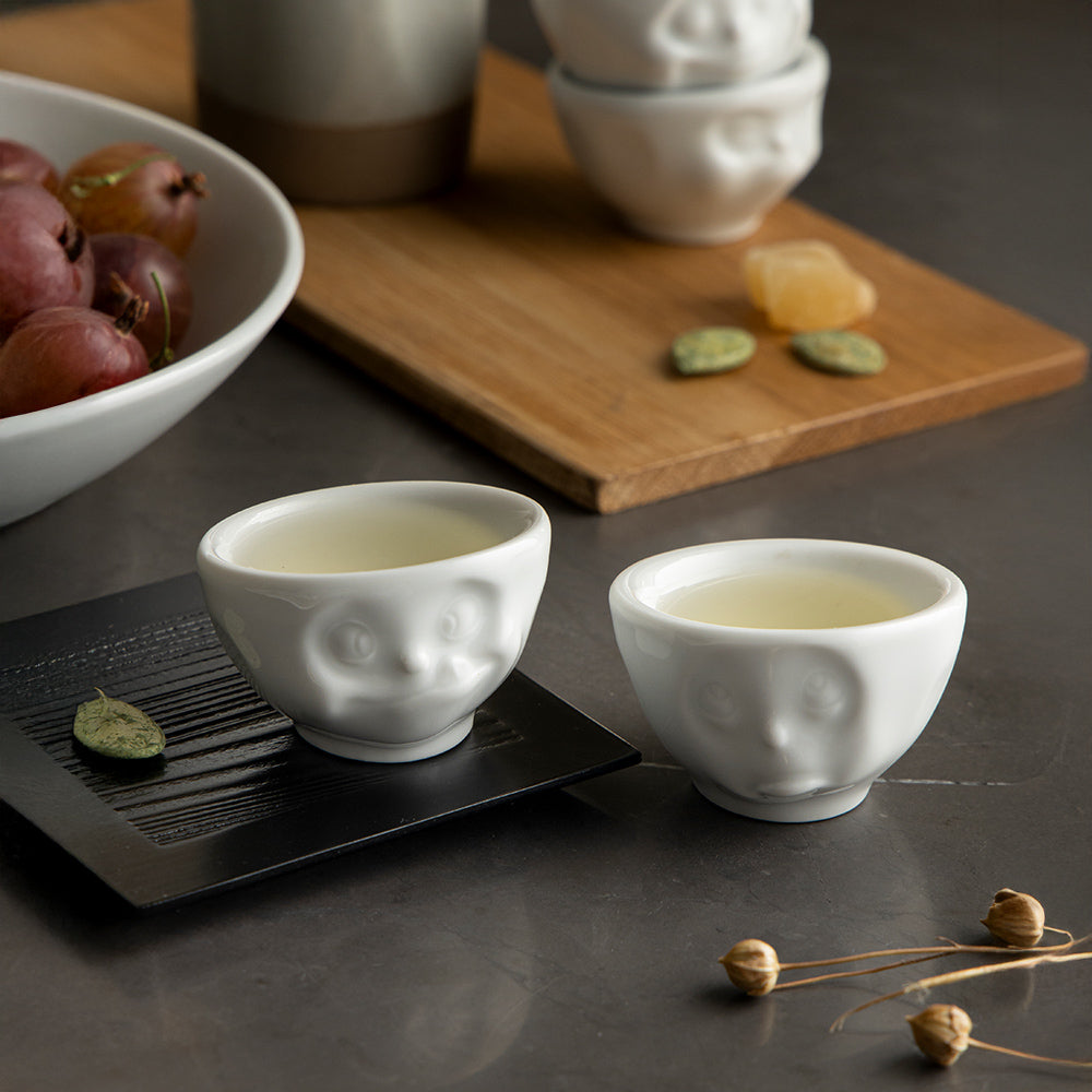 Set of two egg cups in white from the porcelain product family of fun dishware by FIFTYEIGHT Products. Set features two egg cups in white, featuring 'Oh please' and 'tasty' facial expressions. Dishwasher and microwave safe bowls. Shipped in exclusively designed gift box.