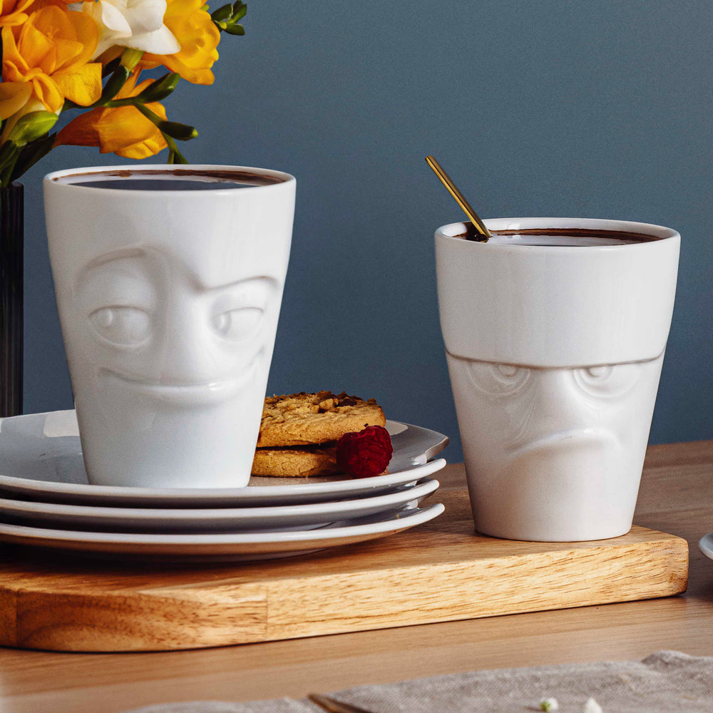Set of two coffee mugs without handles in white from the porcelain product family of fun dishware by FIFTYEIGHT Products. Each offering 11 oz capacity. Dishwasher and microwave safe coffee cups with 'Grumpy' and 'Impish' facial expression. Shipped in exclusively designed gift box.