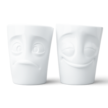 Set of two coffee mugs without handles in white from the porcelain product family of fun dishware by FIFTYEIGHT Products. Each offering 11 oz capacity. Dishwasher and microwave safe coffee cups with 'Cheery' and 'Baffled' facial expression. Shipped in exclusively designed gift box.