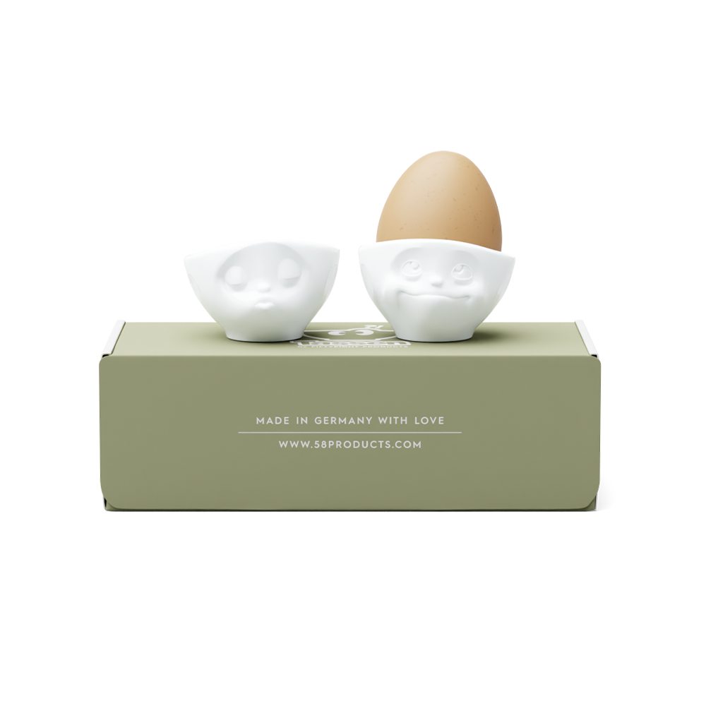 Set of two egg cups in white from the porcelain product family of fun dishware by FIFTYEIGHT Products. Set features two egg cups in white, featuring 'kissing' and 'dreamy' facial expressions. Dishwasher and microwave safe bowls. Shipped in exclusively designed gift box.