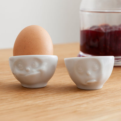 Set of two egg cups in white from the porcelain product family of fun dishware by FIFTYEIGHT Products. Set features two egg cups in white, featuring 'Oh please' and 'tasty' facial expressions. Dishwasher and microwave safe bowls. Shipped in exclusively designed gift box.