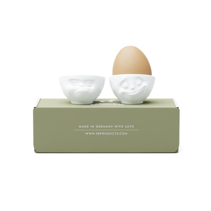 Set of two egg cups in white from the porcelain product family of fun dishware by FIFTYEIGHT Products. Set features two egg cups in white, featuring 'Happy' and 'Hmpff' facial expressions. Dishwasher and microwave safe bowls. Shipped in exclusively designed gift box.