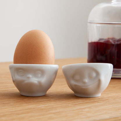 Set of two egg cups in white from the porcelain product family of fun dishware by FIFTYEIGHT Products. Set features two egg cups in white, featuring 'Happy' and 'Hmpff' facial expressions. Dishwasher and microwave safe bowls. Shipped in exclusively designed gift box.